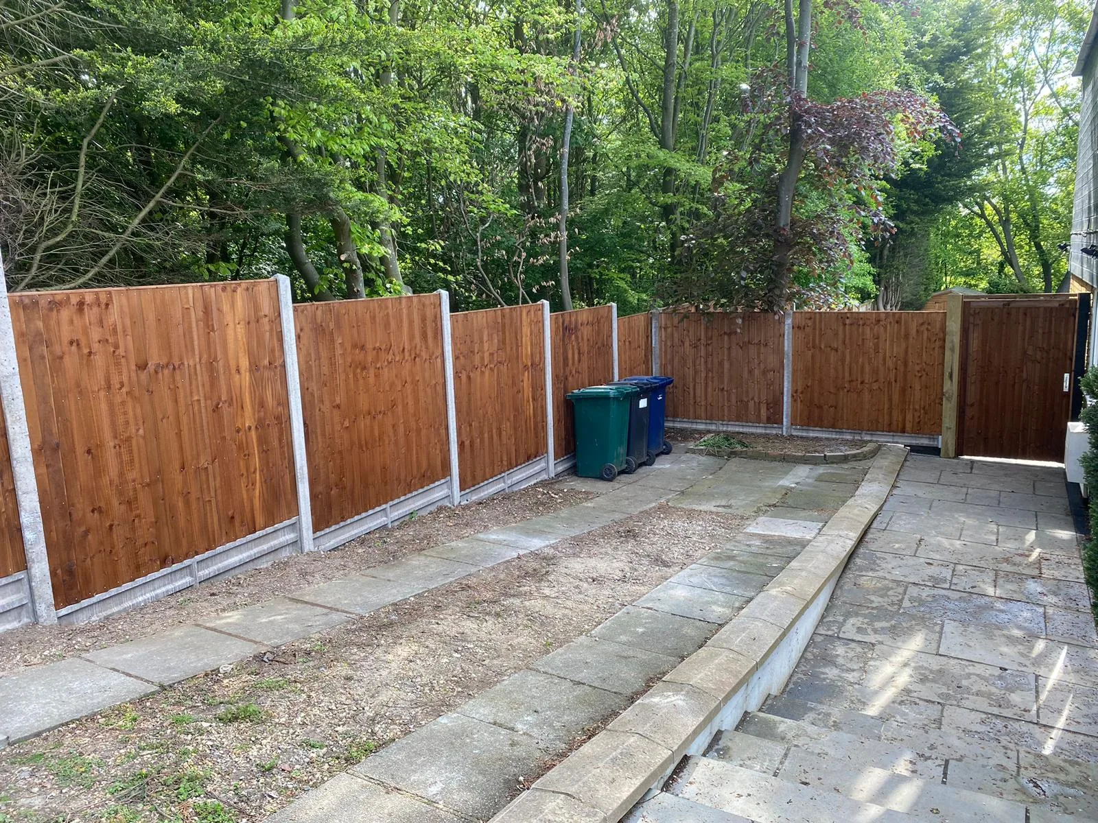 Patios 1 New closeboard fence panels with concrete gravel boards and posts on a sloped garden.